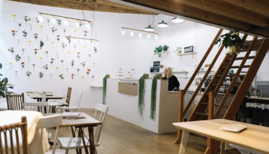 photo de l'intérieur du café, un lieu très simple avec du mobilier en bois et des murs blanc décoré de rangées de fleurs séchées colorées. on y voir également un escalier en bois clair ainsi que le bar