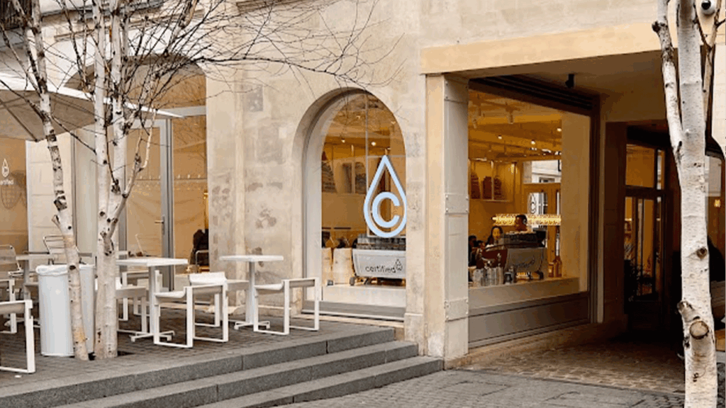 terrasse de cafe a paris avec une grande baie vitrée, des tables et le logo du cafe