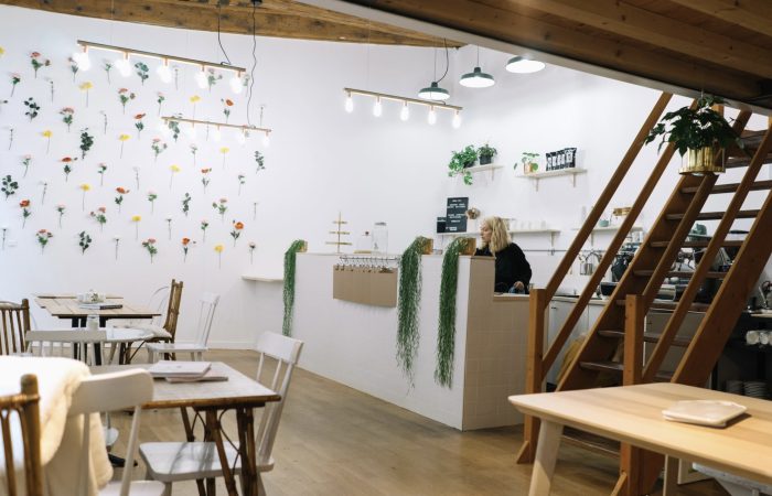 photo de l'intérieur du café, un lieu très simple avec du mobilier en bois et des murs blanc décoré de rangées de fleurs séchées colorées. on y voir également un escalier en bois clair ainsi que le bar