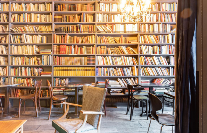 Façade remplie de livre dans le café derrière des tables et des chaises en bois