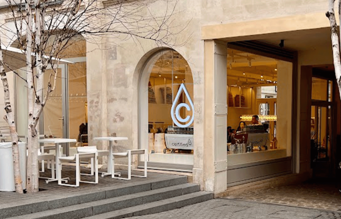 terrasse de cafe a paris avec une grande baie vitrée, des tables et le logo du cafe
